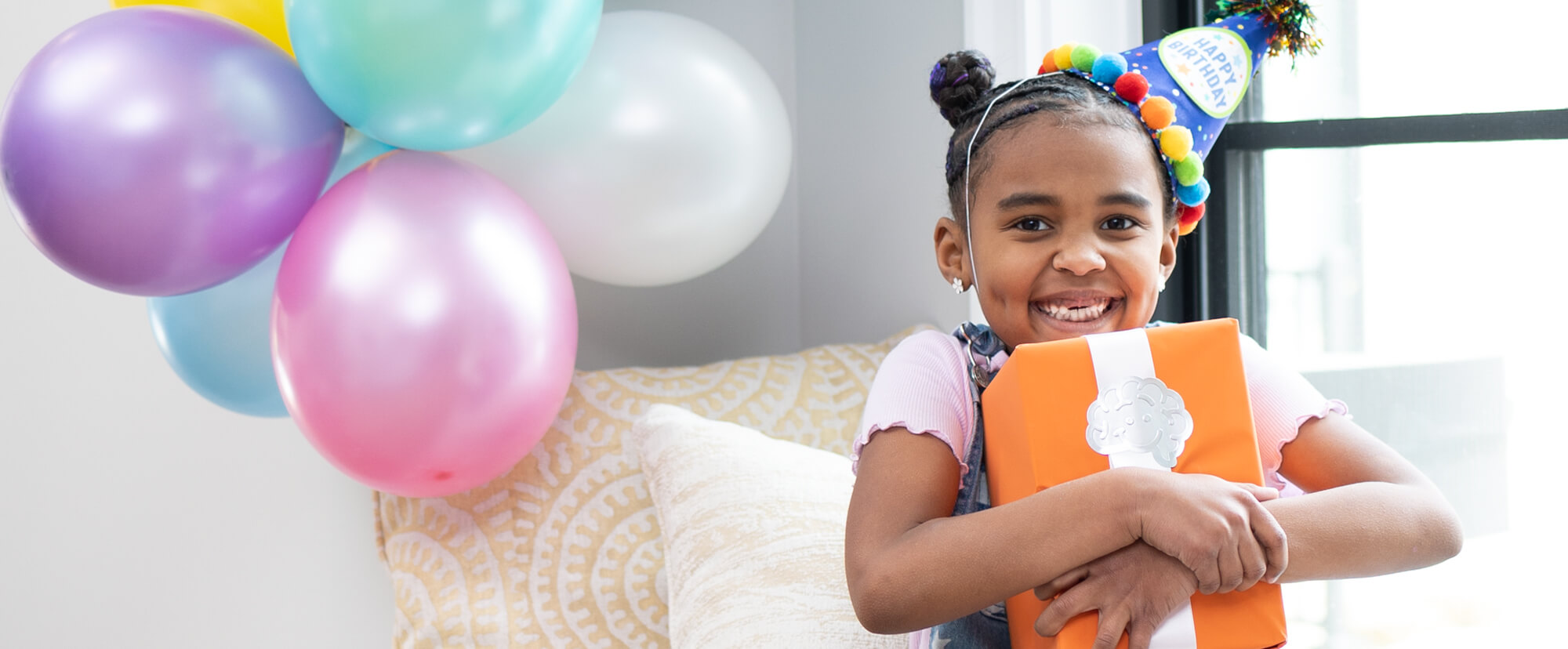 Image of a young girl at a birthday party wearing a birthday hat and holding a birthday present from Fat Brain Toys