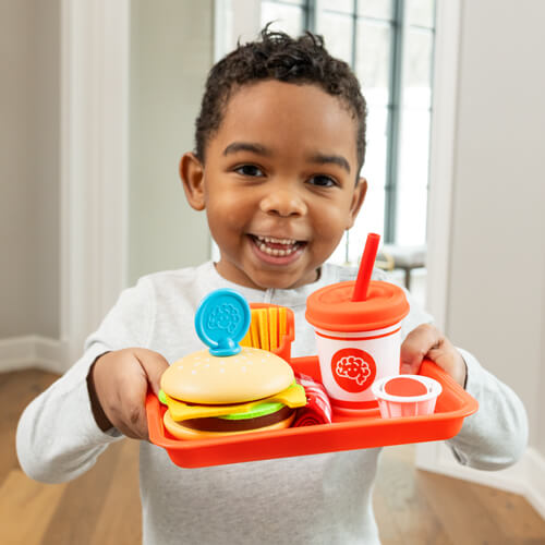 Child smiling and playing with Pretendables Burger & Fries