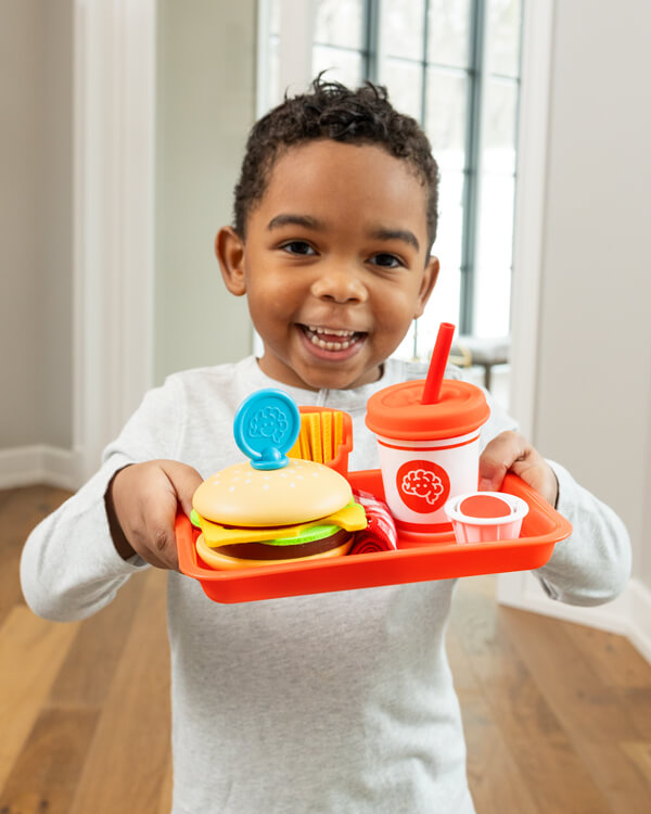 Child smiling and playing with Pretendables Burger & Fries